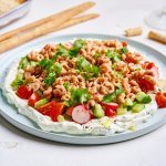 Op een rond groot bord is de dip uitgesmeerd, een witkleurige. Als topping kozen we voor verse knapperige groentjes zoals snackkomkommer, radijzen, kerstomaatjes en lente-ui. Als laatste werken we het geheel af met versgepelde garnalen en verse kruiden. 