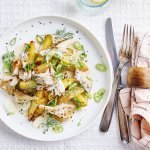 Een heerlijk bordje aardappelsalade staat op tafel, wij serveren hem met stukjes makreel en lente-ui. Om af te werken combineren we hem met een mosterdsausje op basis van yoghurt en mayo. Er ligt bestek langs en roze servette met blauwe lijntjes.