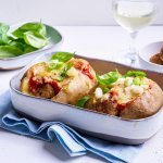 Op tafel staat een ovenschotel met hierin twee gepofte aardappelen, ze zijn gevuld met balletjes en tomatensaus. Ze kregen nog een kaaskorstje, lente-uiringen en basilicum. 