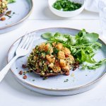 Op een lichtblauw bordje ligt een gevulde champignon met croutons, spek, courgette en verse kruiden. We serveren hem met een portie rucola.