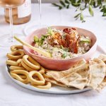 Tijd voor aperitief! Er staat een bordje op tafel met hierop een roos kommetje. In dit kommetje zit de dip op bais van verschillende kazen en krokante ham. Op het bord liggen crackers en stukjes plat brood. Er staan ook glazen rosé langs om de apero goed in te zetten.