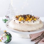 Op taartschaal ligt een pavlova gemaakt met een shotje koffie. Hij is afgewerkt met slagroom, stukjes appel en chocoladeschilfers. 