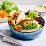 In een blauw kommetje liggen twee pita's, elk pitabroodje is gevuld met groenten en een homemade visburger. we werken af met een sausje op baisis van yoghurt, mayo en curry. 
