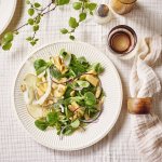 Een mooi wit bordje gevuld met een groene salade, gecombineerd met appel, venkel en oude kaas. Klaar om aan tafel te gaan. 