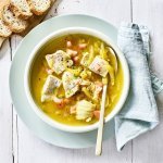 Een soepbord gevuld met warme soep, die er nog eens fantastisch uitziet door de kleurrijke stukjes groenten, vis en kruiden. Er ligt ook nog wat gesneden brood langs, om de laatste drup op te likken. 