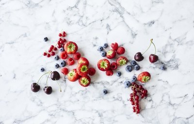 Aardbeien, frambozen, blauwe bessen, rode bessen en kersen liggen op een marmer aanrecht. Klaar om te verwerken in een homemade confituur. 