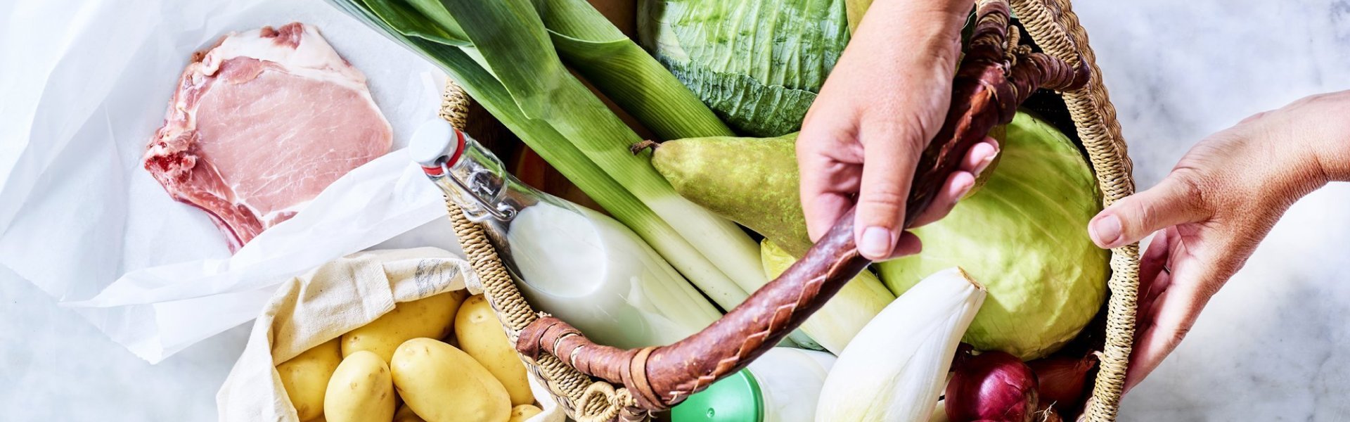 Mand staat op het aanrecht en is gevuld met heerlijke producten van eigen bodem. Denk maar aan prei, witte kool, witloof, yoghurt, uien, krieltjes, varkensvlees... Klaar om meteen aan de slag te gaan. 